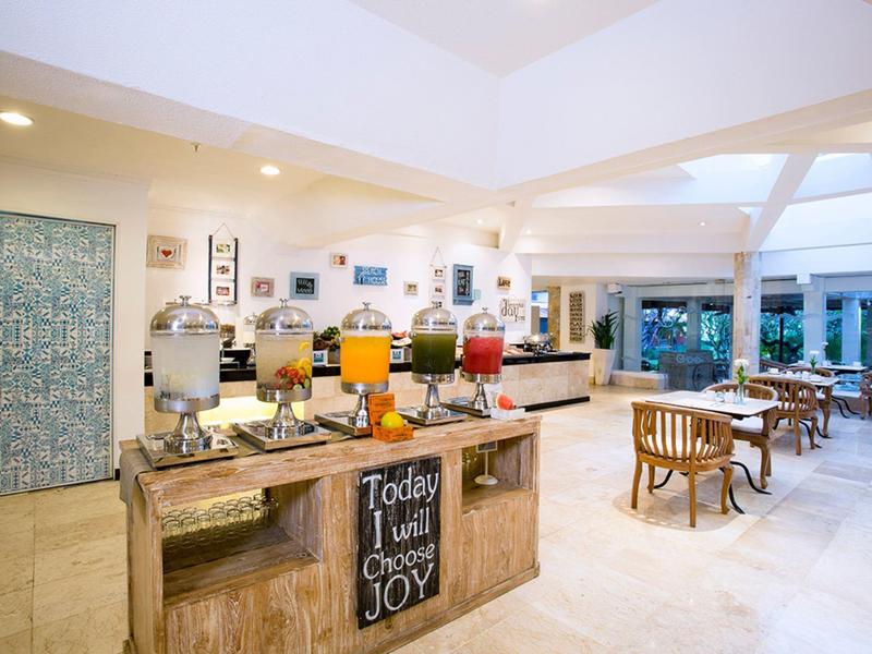 Interno spazioso di un hotel con buffet di succhi colorati e tavoli in legno chiaro.