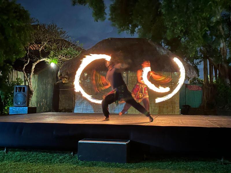 Spettacolo di fuoco serale su palco all'aperto con vegetazione intorno.