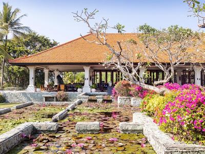 Un hôtel tropical avec un étang rempli de nénuphars et des buissons fleuris au premier plan.