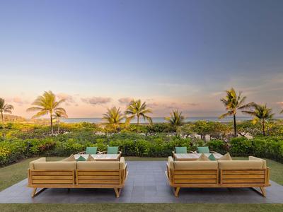 Zwei moderne Sofas mit Kissen auf einer Terrasse mit Blick auf tropische Pflanzen und das Meer bei Sonnenuntergang.