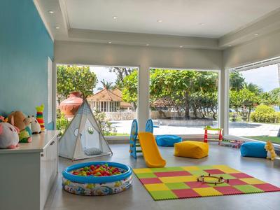 Salle de jeux lumineuse pour enfants avec piscine à balles, toboggan, tente et tapis coloré avec vue sur la verdure.