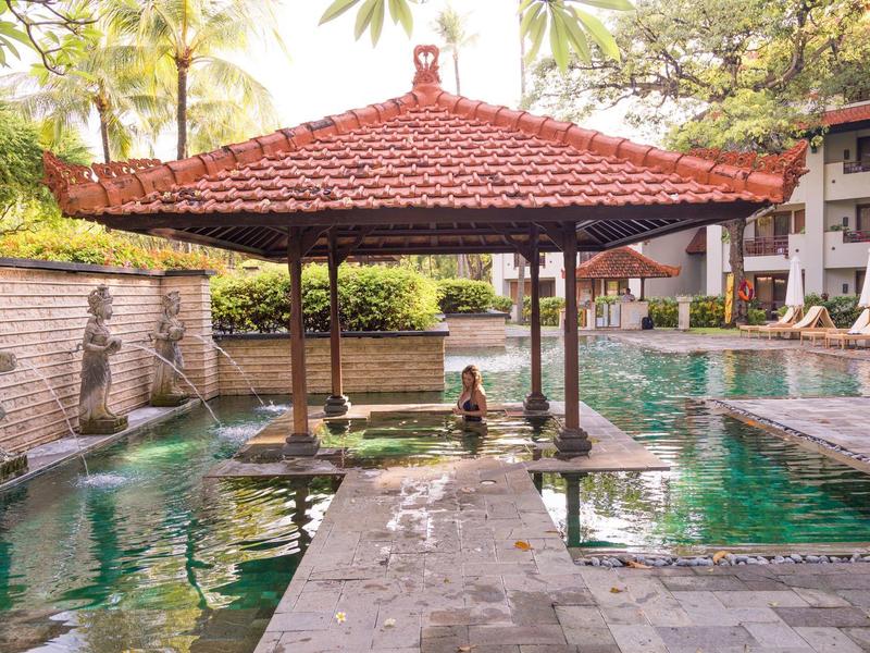 Piscine avec pavillon rouge traditionnel et palmiers dans un complexe hôtelier.