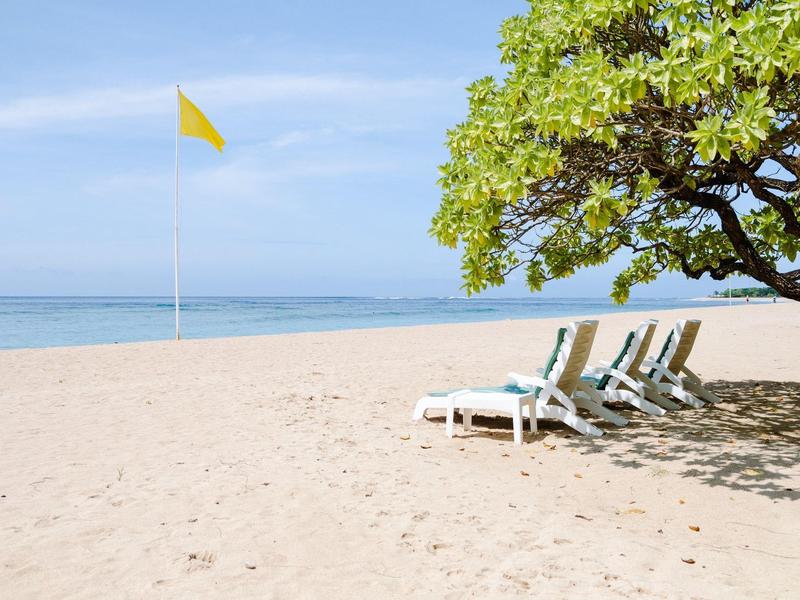 Chaises longues vides à côté d'un arbre sur une plage de sable calme avec un drapeau jaune.