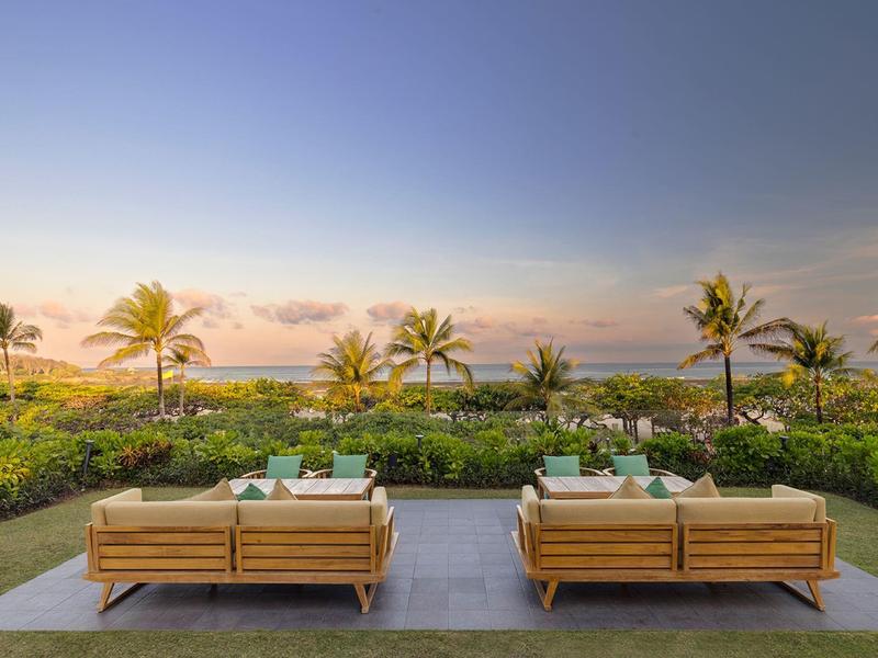 Deux bancs modernes sur une terrasse avec vue sur des palmiers tropicaux et la mer au coucher du soleil.