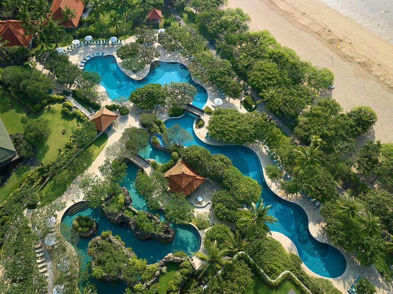 Vue aérienne d'une piscine de complexe avec jardin tropical près d'une plage de sable.
