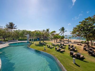Poolbereich mit Liegestühlen und Blick auf den Strand unter blauem Himmel