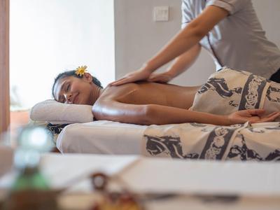 Zrelaksowana kobieta otrzymuje masaż pleców w jasnym gabinecie spa.