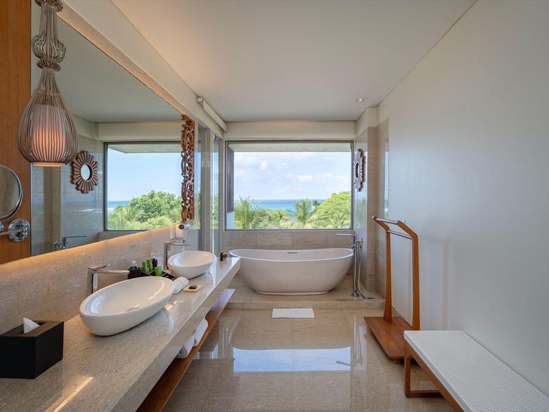 Nowoczesna łazienka z wolnostojącą wanną, podwójnymi umywalkami, dużym lustrem i widokiem na ocean przez okno.