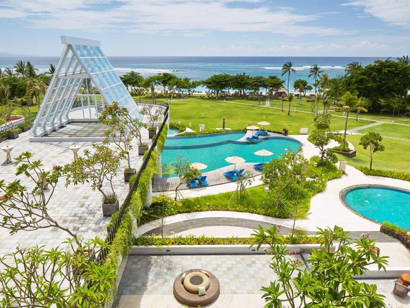 Widok na nowoczesny basen z oceanem w tle, otoczony zielenią.