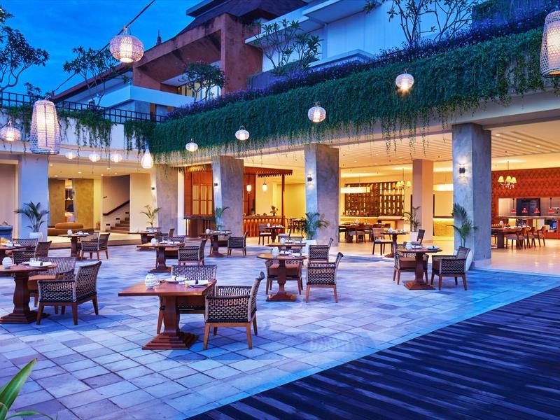 Hotelowy taras na zewnątrz z stołami, krzesłami, światełkami i barem pod niebieskim zmierzchem.