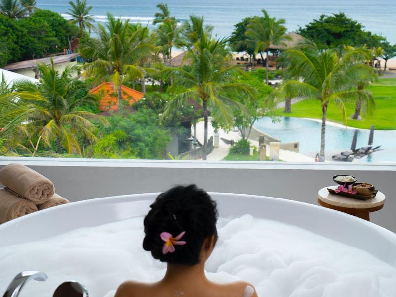 Osoba relaksująca się w kąpieli z pianą z widokiem na ocean i tropikalne otoczenie.