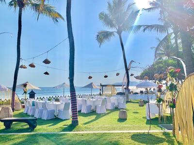 A festively decorated beach patio with white chairs and tables under palm trees in sunshine.