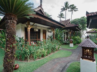Bungalós tradicionales con camino pavimentado y vegetación tropical en un jardín de hotel.