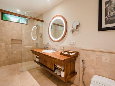 Baño moderno con espejo redondo iluminado, mueble de madera y ducha a nivel del suelo.