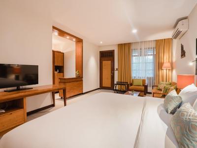 Habitación de hotel luminosa con cama grande, televisión de pantalla plana, muebles de madera y ventana con cortinas.