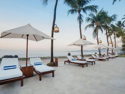 Beach hotel with sun loungers and umbrellas among palm trees by calm sea