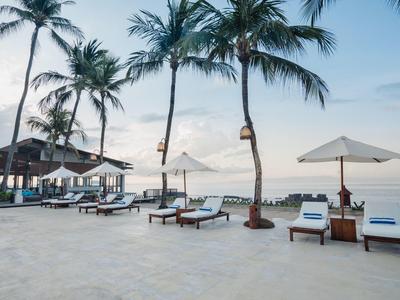 Resort de playa con tumbonas, sombrillas y palmeras junto al mar al atardecer.