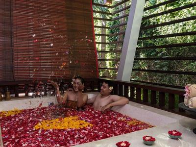 Dos personas disfrutan de un baño lleno de pétalos de flores en un entorno al aire libre con paredes de madera.