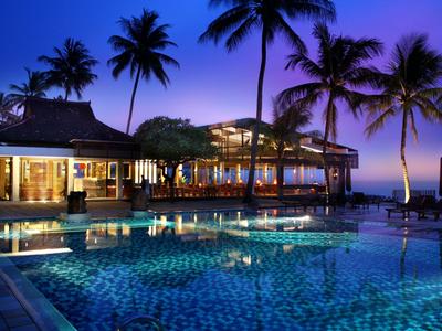 Hotel with illuminated pool and palm trees at sunset by the sea