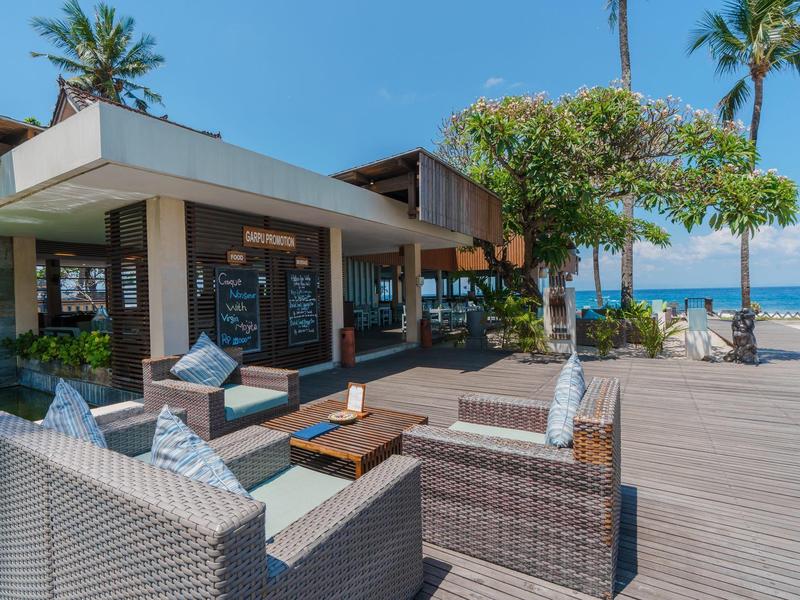 Terraza con muebles de salón modernos y vista al mar y palmeras bajo un cielo soleado
