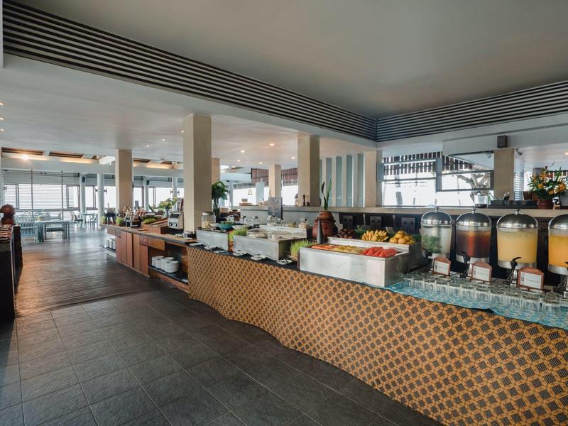 Área luminosa de desayuno con buffet y dispensadores de bebidas en un hotel moderno.
