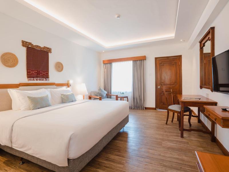 Habitación de hotel luminosa con cama grande, suelo de madera y TV moderna en la pared.