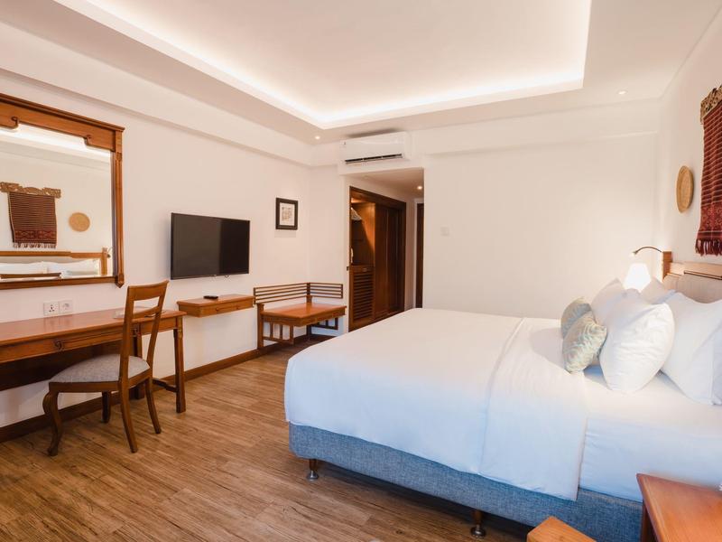 Habitación de hotel luminosa con cama doble, escritorio, televisor y suelo de madera.