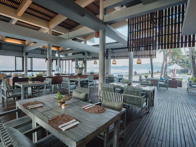 Restaurante moderno con suelo de madera y grandes ventanales con vista a palmeras.