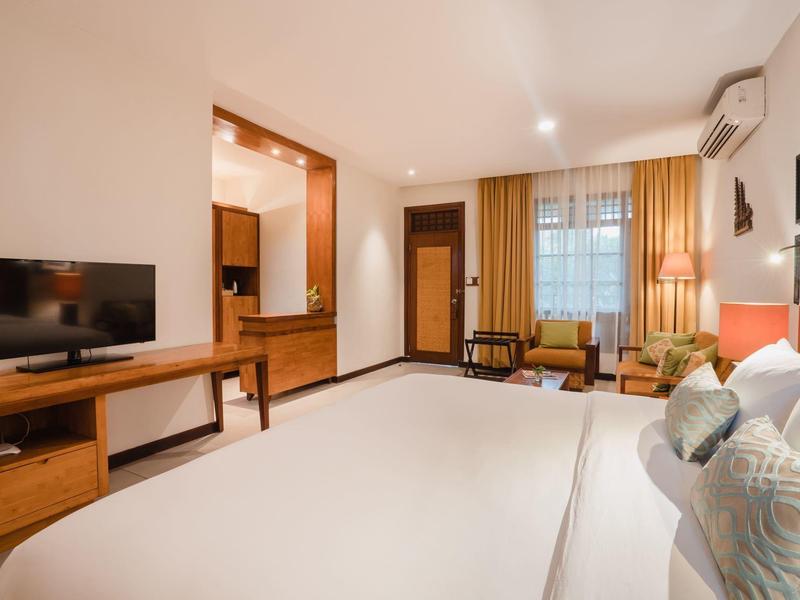 Habitación de hotel luminosa con cama grande, televisión de pantalla plana, muebles de madera y ventana con cortinas.