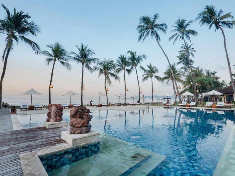 Piscina lujosa con palmeras y vista al mar al atardecer