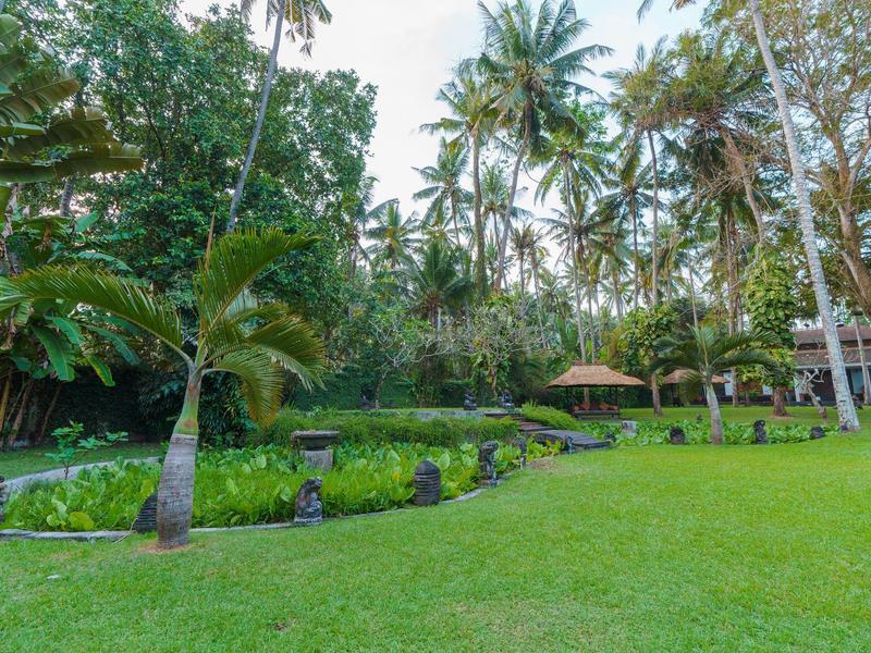 Amplio jardín verde con palmeras y área de descanso en un paisaje tropical junto a un hotel.