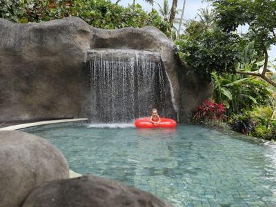 Ein ruhiger Pool mit Wasserfall, umgeben von Felsen und grünen Pflanzen, mit einem roten Schwimmring.