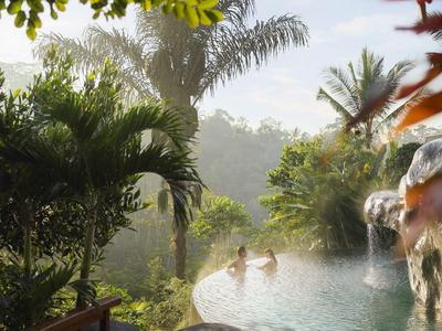 Infinity-zwembad met waterval en tropische begroeiing in een heuvelachtig landschap.