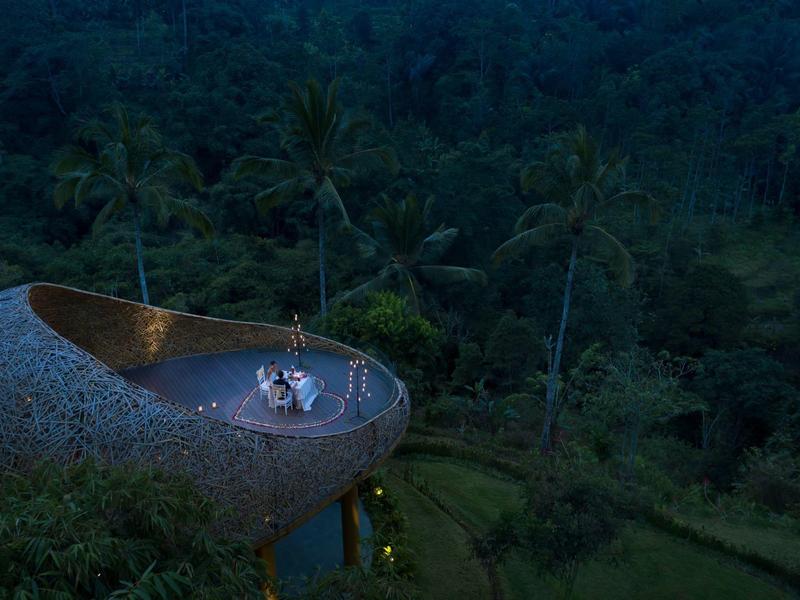 Ein geschwungener Steinpavillon mit Menschen, umgeben von dichtem grünen Dschungel bei Dämmerung.