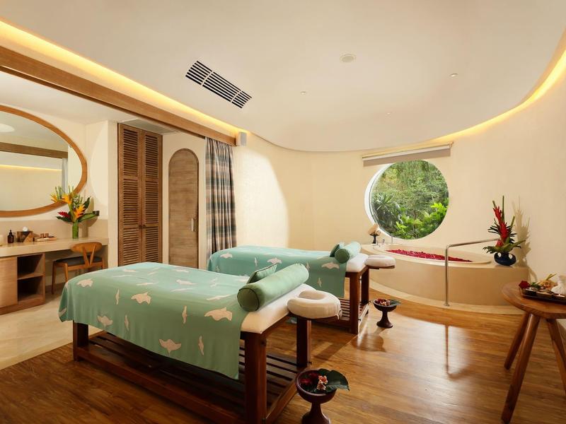 Helles Massageraum mit zwei Betten, runden Fenstern und warmem indirektem Licht.