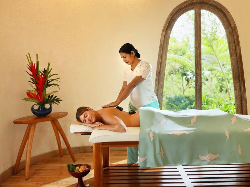 Eine Frau erhält Rückenmassage in hellem Raum mit großem Fenster und Blumendekoration.