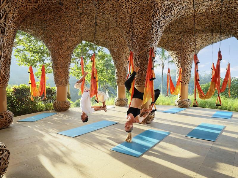 Yoga-Übungen mit Hängematten in einer großen, offenen Halle mit Steinbögen und Blick ins Grüne.