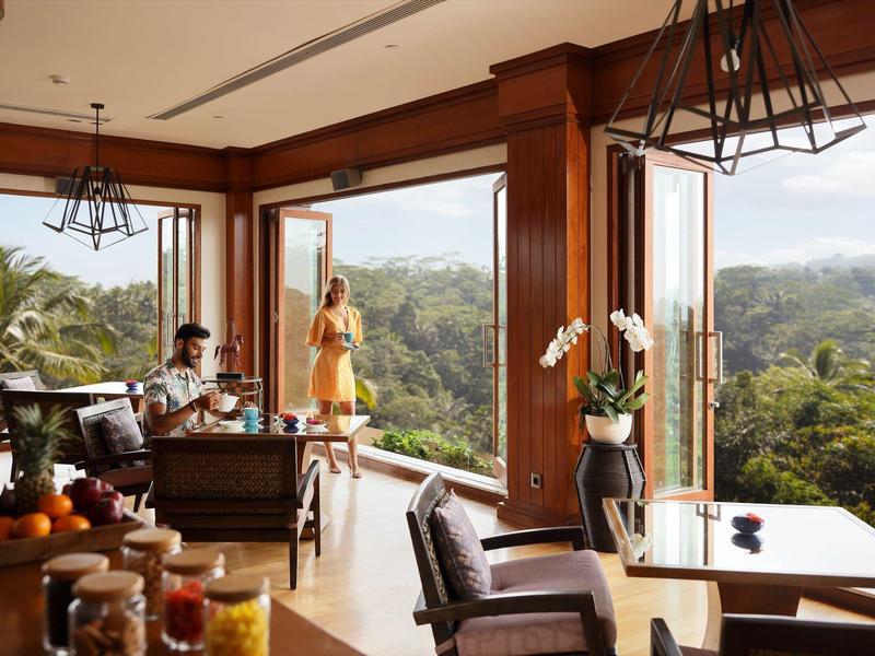 Moderner Wohnraum mit großen Fenstern, Holzmöbeln, Pflanzen und Blick auf grüne Natur.