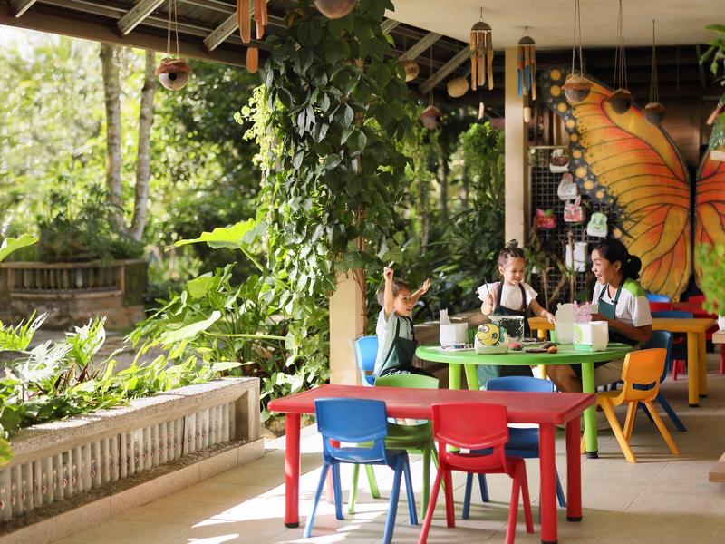 Bunte Kindertische und Stühle auf einer Terrasse mit grünen Pflanzen und einem Schmetterlingsbild.