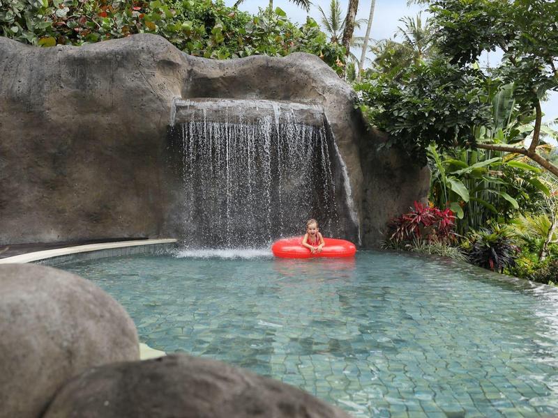Ein ruhiger Pool mit Wasserfall, umgeben von Felsen und grünen Pflanzen, mit einem roten Schwimmring.