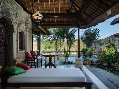 Pohodlná veranda s denní postelí, polštáři a výhledem na zahradu a palmy při západu slunce.