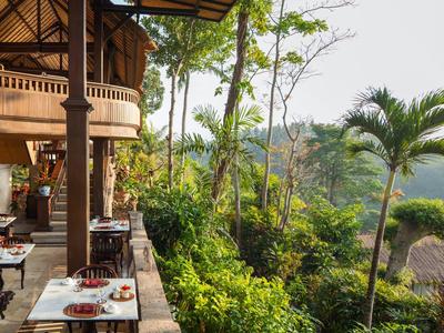 Otevřená restaurace s dřevěnou podlahou, stoly vedle tropické zahrady s výhledem na údolí.