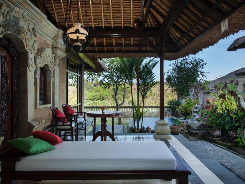 Pohodlná veranda s denní postelí, polštáři a výhledem na zahradu a palmy při západu slunce.