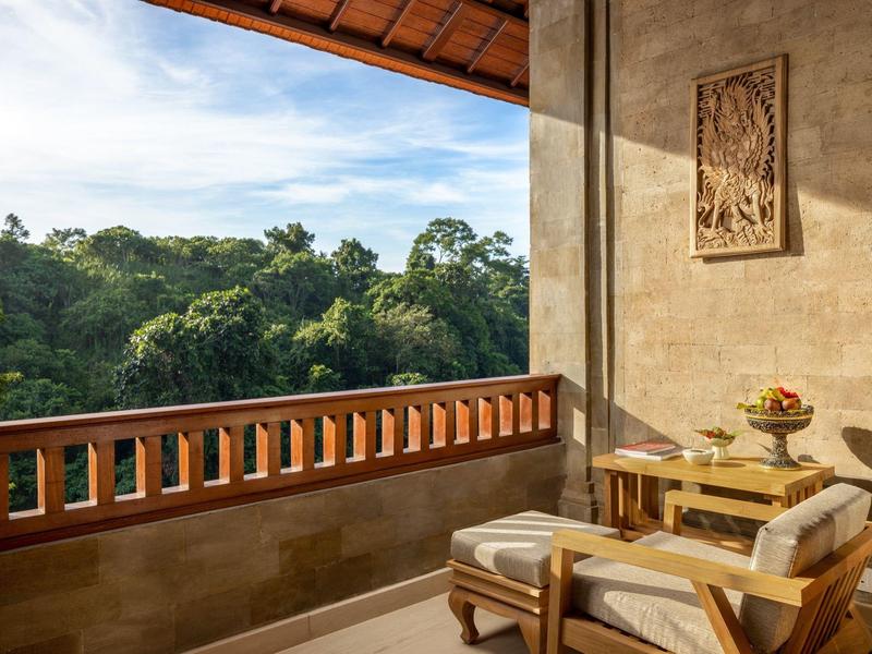 Balkon s pohodlnými křesly s výhledem na zelené stromy pod modrou oblohou.