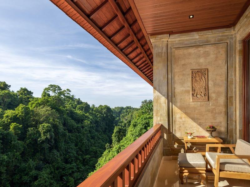 Balkon s židlemi a stolem s výhledem na hustý zelený les a modrou oblohu.