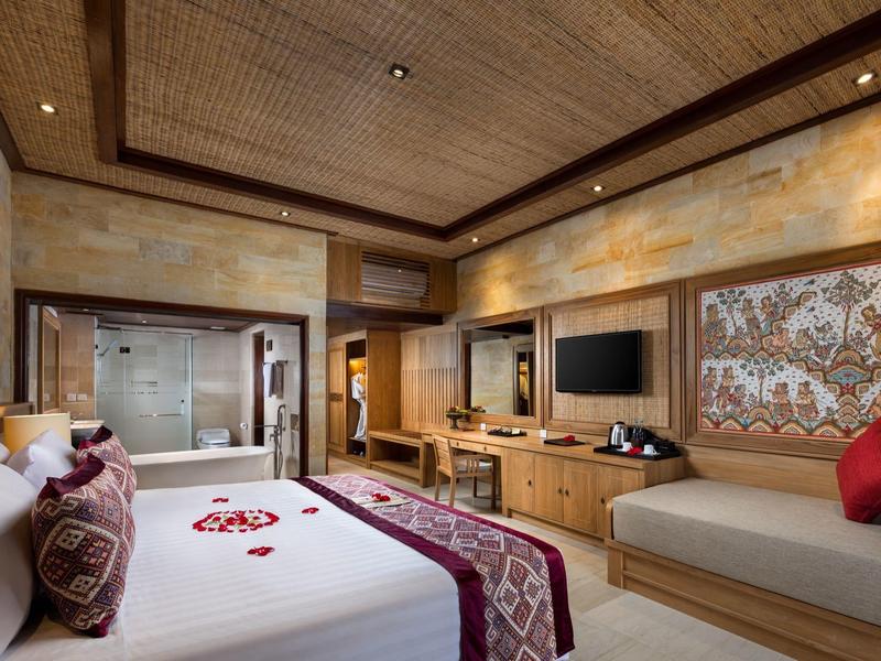 Luxusní hotelový pokoj s velkou postelí, pohovkou, dřevěným stropem a moderním zábavním systémem.