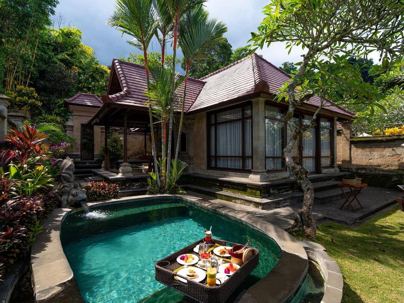 Tradiční vila s bazénem a tropickou zahradou pod zataženou oblohou.