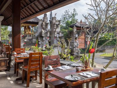 Terras van een hotel met houten tafels en stoelen, gedekt voor gasten met uitzicht op stenen tempelbeelden.