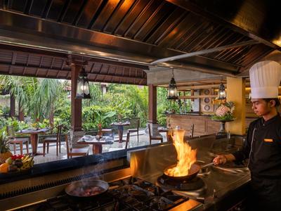 Kok met hoed kookt in open hotelkeuken met uitzicht op terras en tuin.