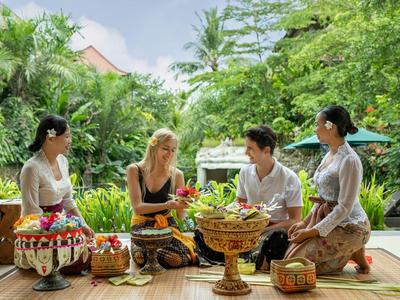 Vier mensen zitten buiten in een tropische omgeving met traditionele manden en versieringen.